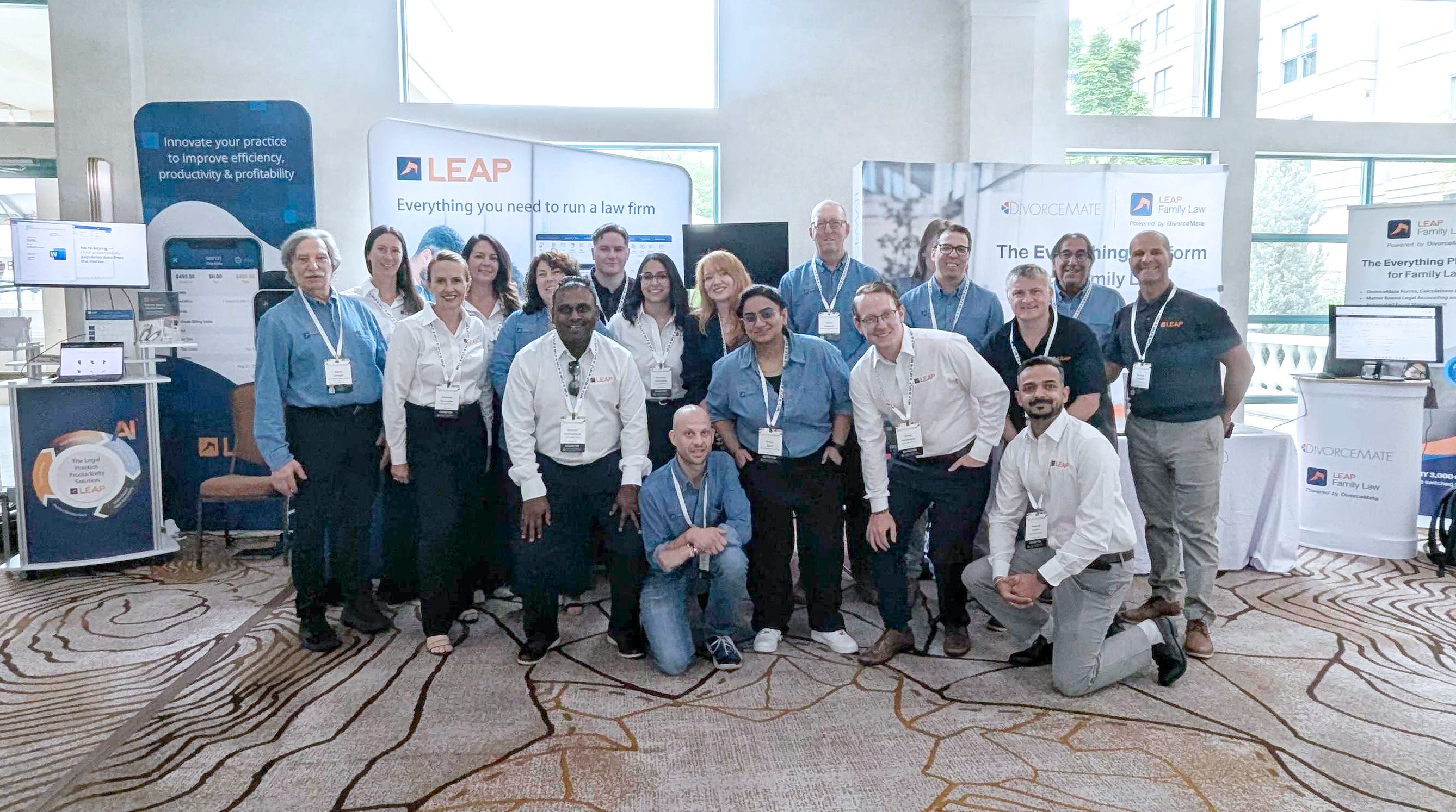 Group of people posing in front of LEAP exhibition booth, wearing name tags, in an event setting with promotional banners and displays.