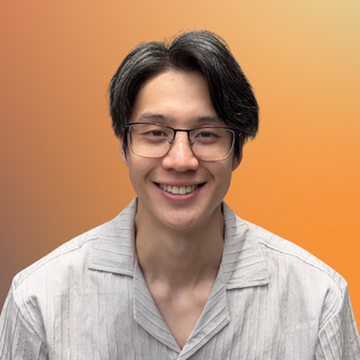 Smiling person with glasses and short hair wearing a light gray shirt. Warm gradient background.