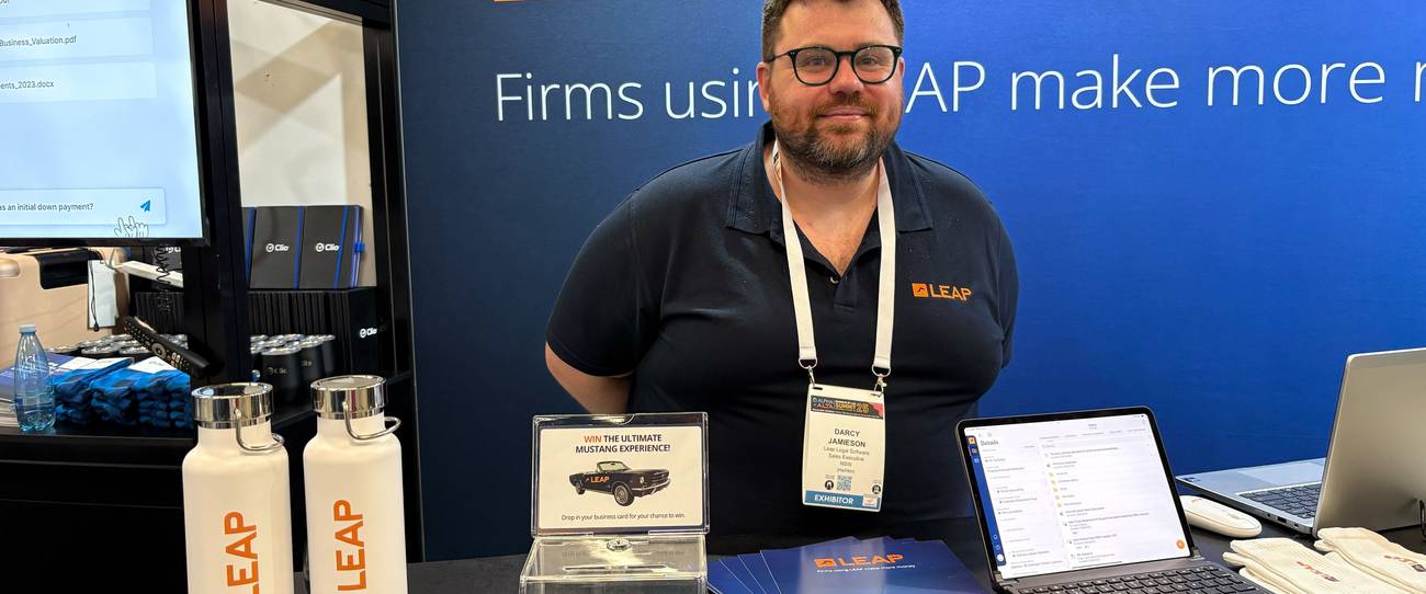 A man stands at a LEAP booth with branded merchandise, including water bottles and brochures, beside a laptop displaying information.
