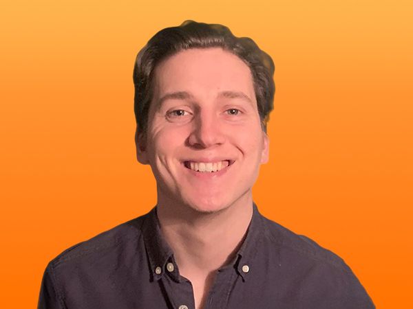 Smiling person with short hair wearing a dark shirt, set against an orange background.