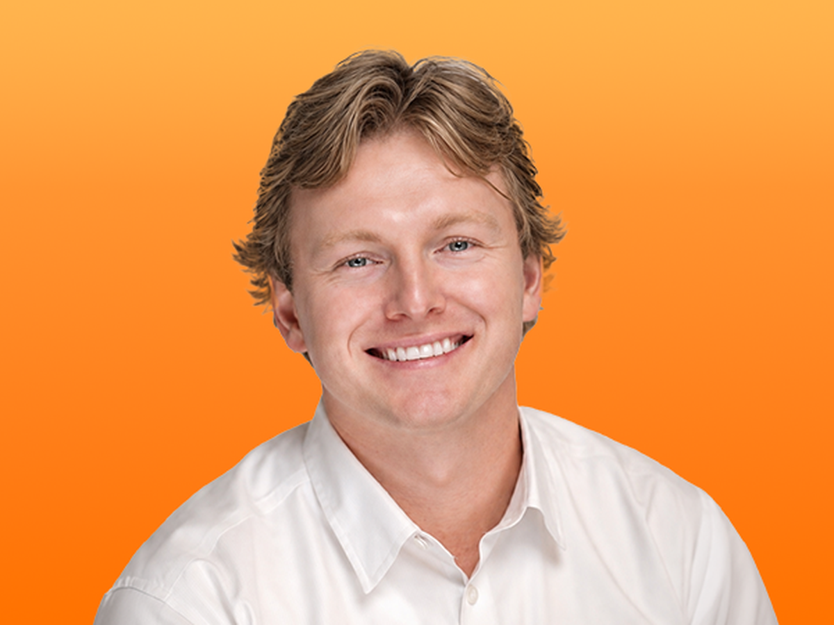 Smiling person with short, wavy hair wearing a white shirt against an orange background.