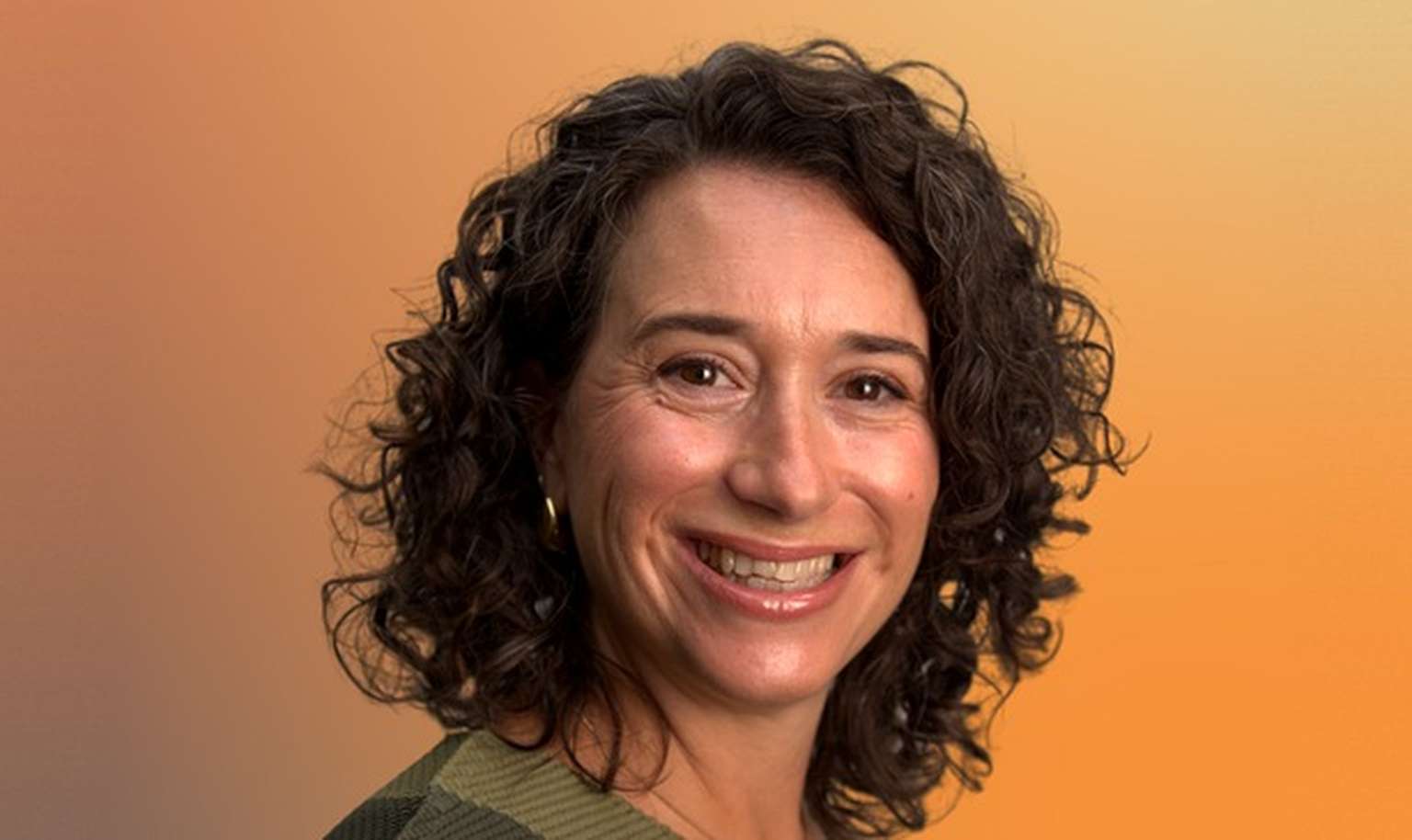 Smiling woman with curly brown hair against an orange gradient background.