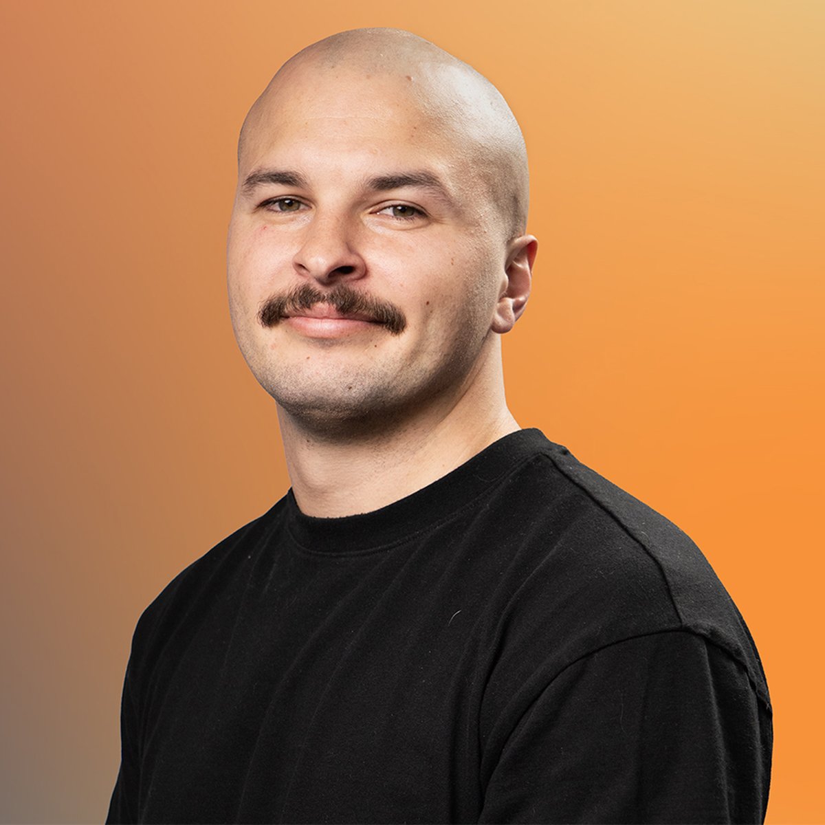 A bald man with a mustache, wearing a black shirt, smiles slightly against an orange gradient background.