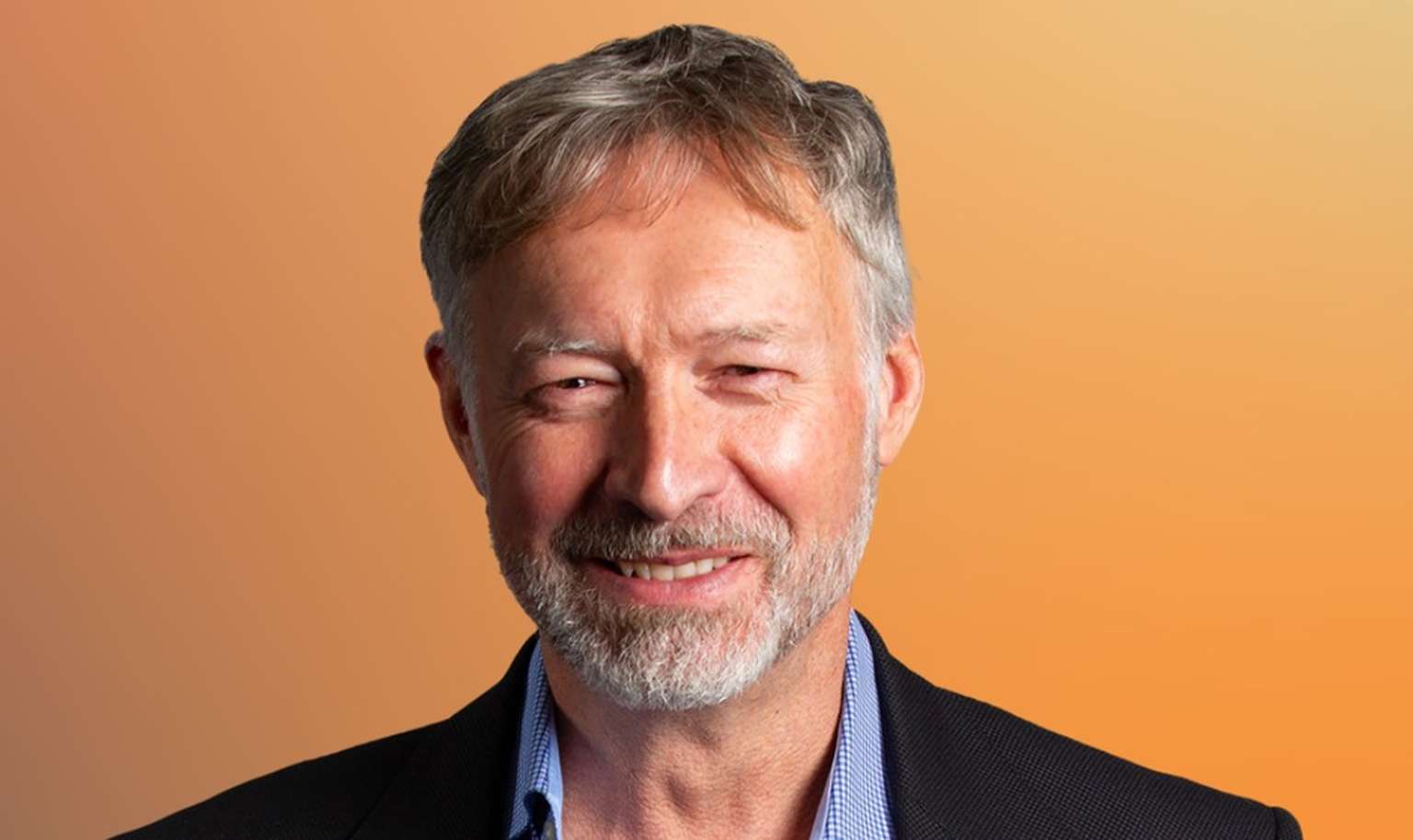 Smiling man with short gray hair and a beard, wearing a suit jacket and shirt, against an orange gradient background.