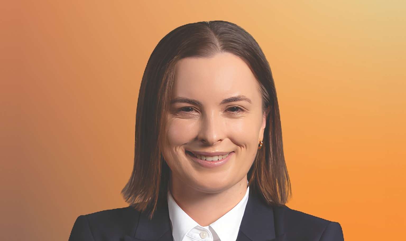 Smiling person with short hair, wearing a dark blazer and white shirt, against an orange gradient background.