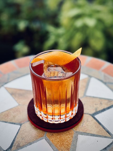 a reddish-brown cocktail with orange twist garnish and big rock of clear ice