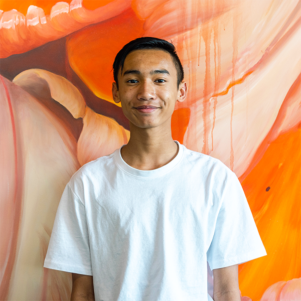 A young man with dark hair in a white shirt stands against a predominantly red artwork