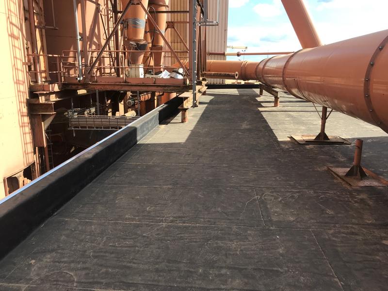 Plat industriedak met zwarte dakbedekking, met oranje buizen op steunen ernaast.