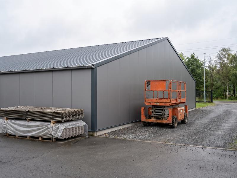 Bedrijfshal met een nieuw metalen dak en nieuwe gevelpanelen, met oude golfplaten op een pallet en een hoogwerker ernaast