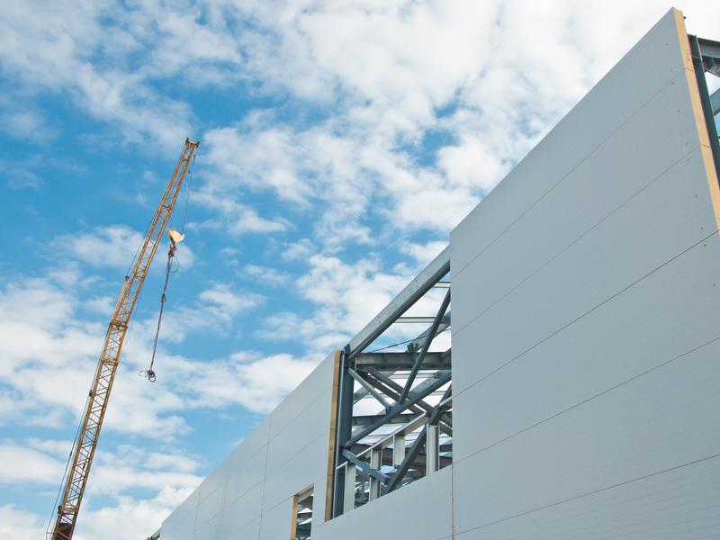 Witte gevelpanelen op een stalen skelet, met een kraan ernaast