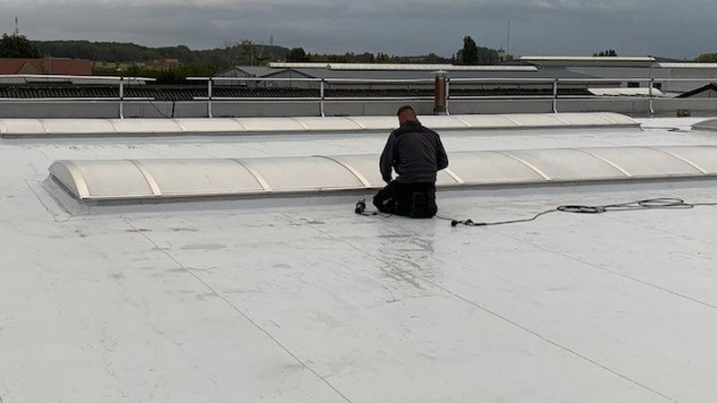 Werker knielt naast een rij gebogen lichtstraten op een wit plat dak