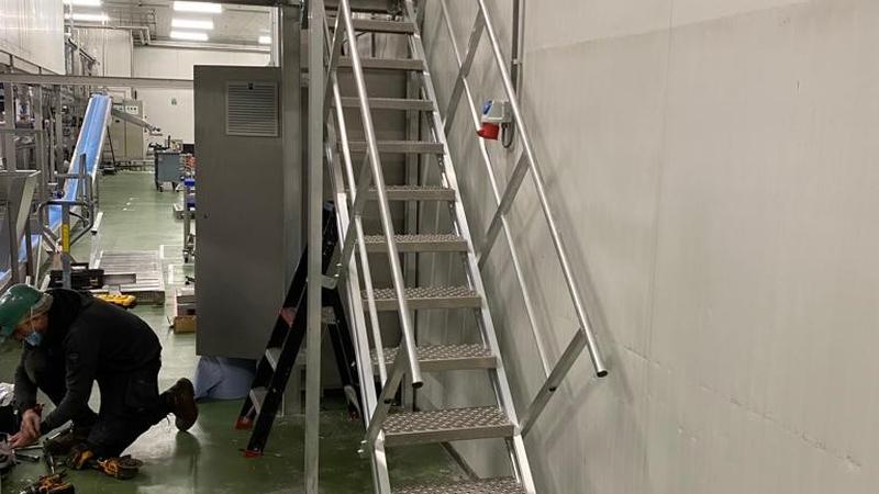 Aluminium trap met leuningen naar een bordes in een productiehal, met gereedschap op de vloer