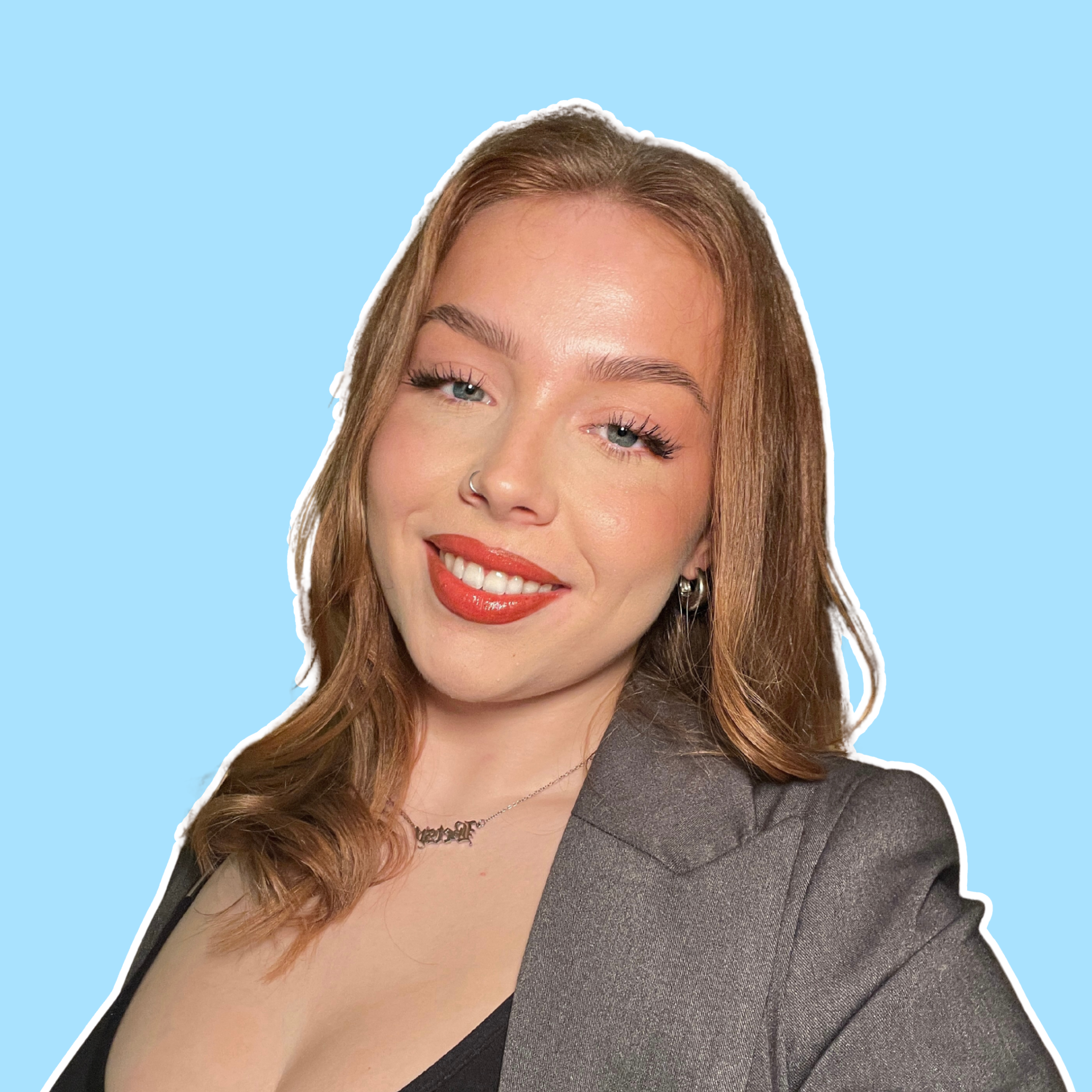 Smiling person with reddish-brown hair and red lipstick, wearing a dark jacket against a light blue background.