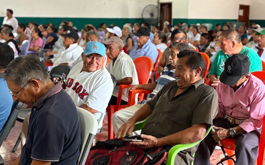 A group of elderly people seated in a community hall, engaging in a lively discussion.