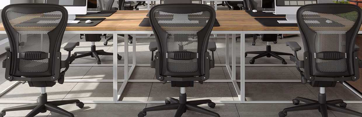 Modern office space with three ergonomic chairs facing large wooden desks, equipped with computers and black desk mats.