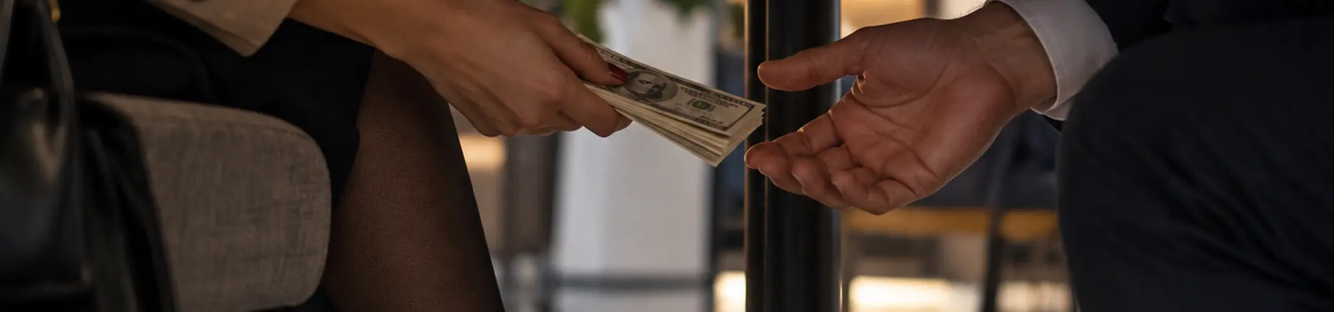 Two people discreetly exchange cash under a table, depicted from a low angle.