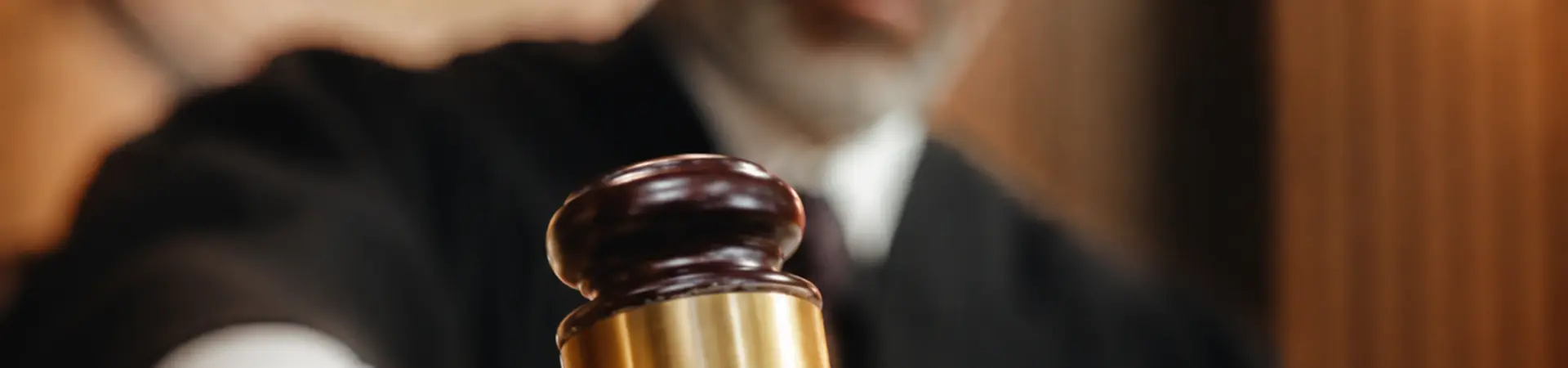Judge striking a gavel in a courtroom, showing authority and decision-making. The image focuses on the gavel, with the judge blurred in the background.