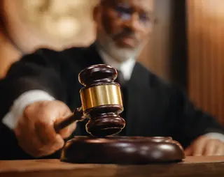 Judge striking a gavel in a courtroom, showing authority and decision-making. The image focuses on the gavel, with the judge blurred in the background.