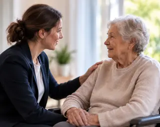Een jonge vrouw praat vriendelijk met een oudere vrouw in een rolstoel, terwijl ze haar schouder aanraakt. Ze glimlachen naar elkaar.
