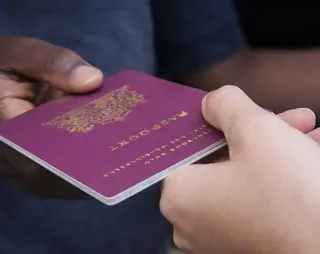 Two hands exchanging a maroon passport.