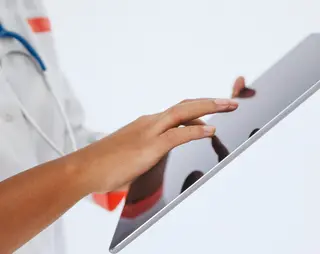 Een dokter met witte doktersjas houdt een grote tablet vast