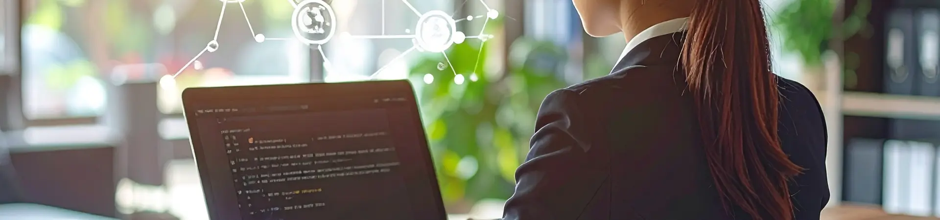A woman in a business suit works on a laptop with digital icons floating above, in a sunlit office.