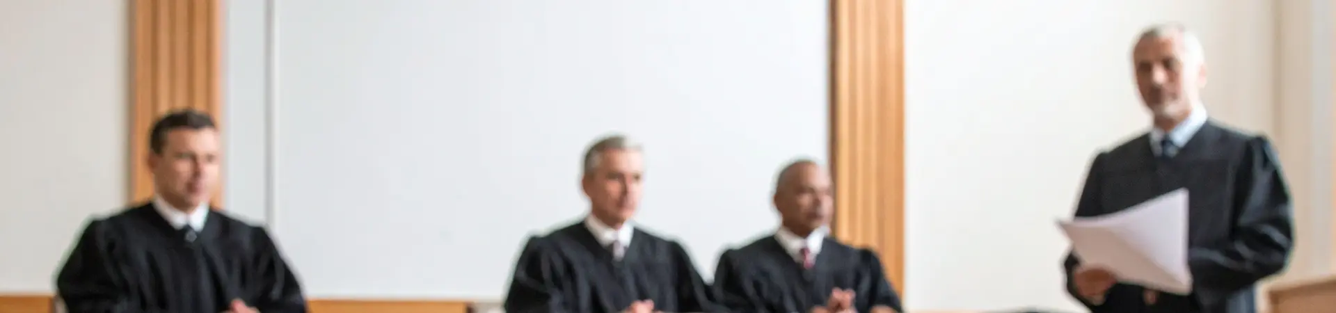 A courtroom with a gavel in the foreground, and four judges in robes seated at a bench in the background.