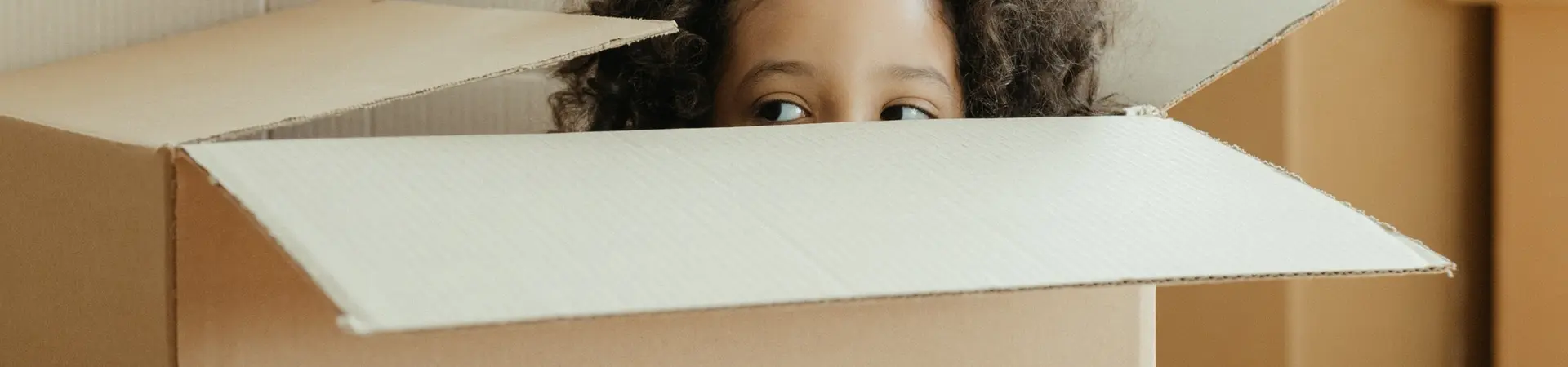 Verhuisdozen waarbij een klein meisje in een verhuisdoos verstopt zit