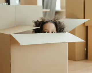 Verhuisdozen waarbij een klein meisje in een verhuisdoos verstopt zit