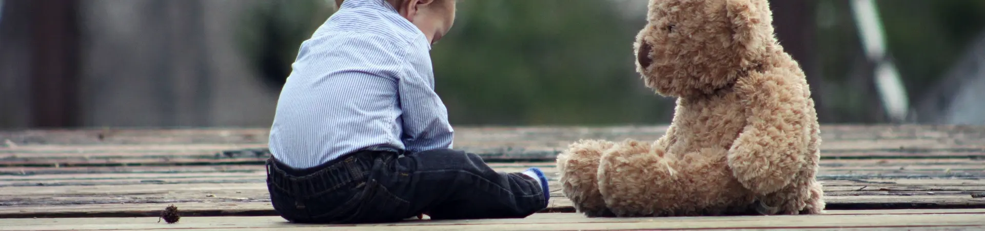 Kind zit met grote knuffelbeer op een vlonder