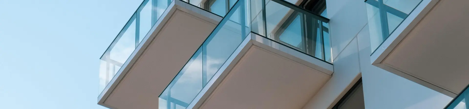 Een modern en strak appartementencomplex met veel balkons op een zonnige dag. 