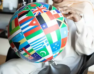 Een vrouw houdt op haar schoot een kleurrijke wereldbol met hierop verschillende vlaggen van landen vast