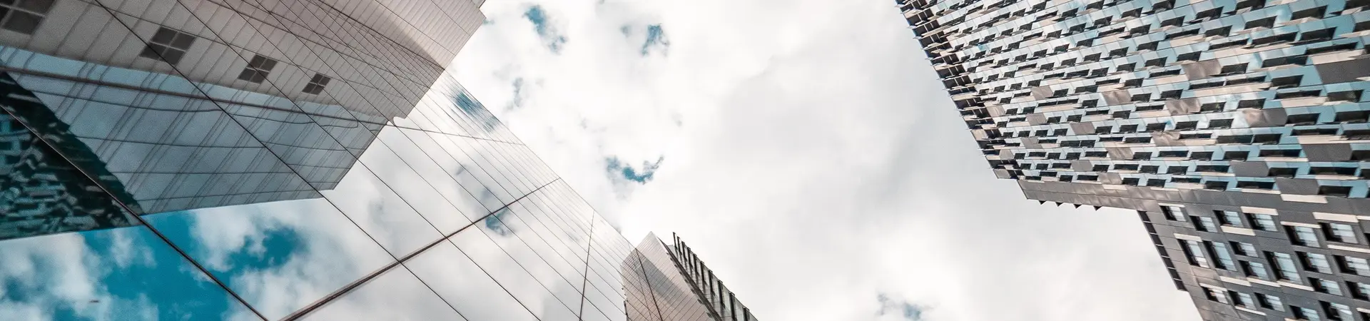 Grote gebouwen in een stad met weerspiegeling van de wolken in een van de hoge gebouwen je kijkt van onderaf het gebouw richting de wolken.