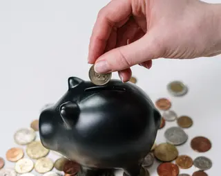Vrouw stopt geld in een zwart spaarvarken.