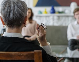 Mediator met kort haar zit met haar rug naar de camera en is in gesprek met een scheidend koppel.