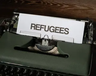 Typemachine met een pagina met de tekst Refugees vluchtelingen