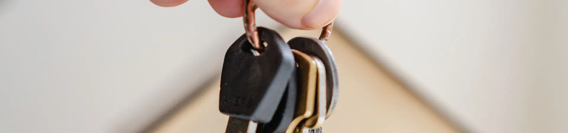 Een sleutelbos wordt vastgehouden na koop of verkoop roerende of onroerende zaken. Op de achtergrond zie je een houten huisje. 