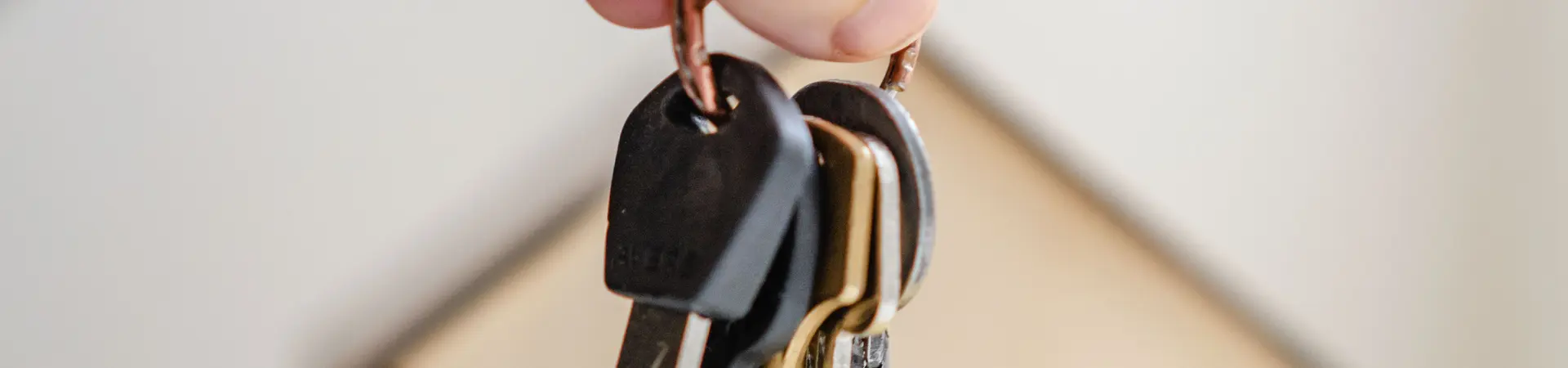 Een sleutelbos wordt vastgehouden na koop of verkoop roerende of onroerende zaken. Op de achtergrond zie je een houten huisje. 