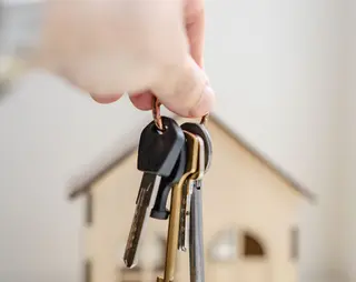 Een sleutelbos wordt vastgehouden na koop of verkoop roerende of onroerende zaken. Op de achtergrond zie je een houten huisje. 