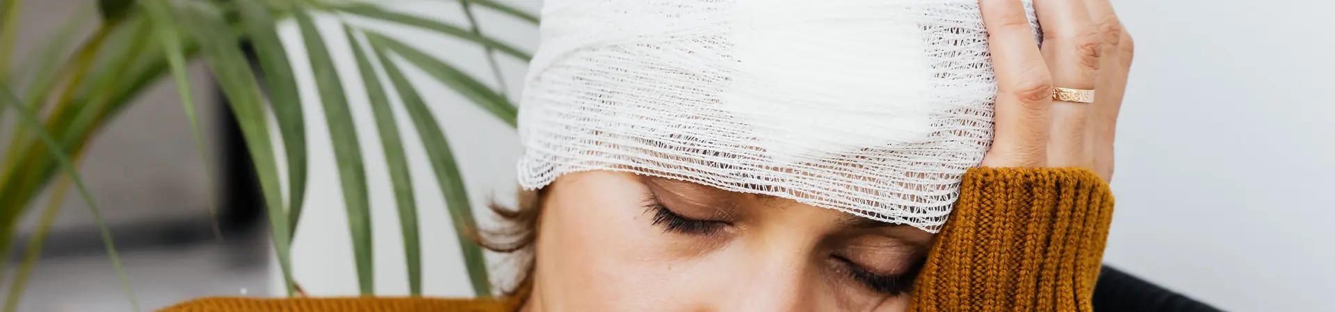Vrouw met verband om haar hoofd zit op de bank en kijkt verdrietig