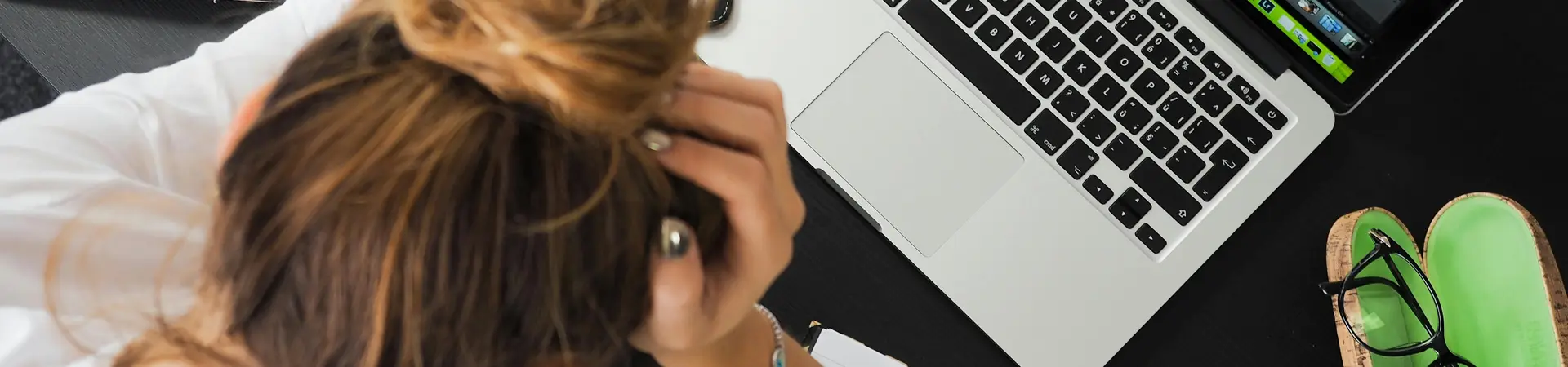 Meisje zit achter bureau met laptop agenda telefoon en heeft haar handen op haar hoofd en ervaart stress