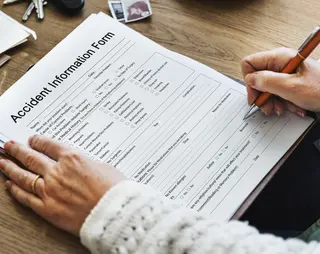 Letselschadeformulier wordt door een vrouw aan een houten bureau ingevuld met een rode pen