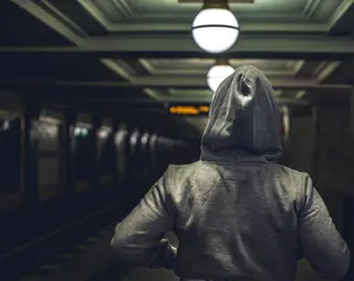Een persoon in een donkere ruimte met een hoodie aan met capuchon op zijn hoofd