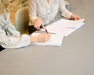 Arbeidsovereenkomst wordt door twee vrouwen aan tafel ondertekend met een pen