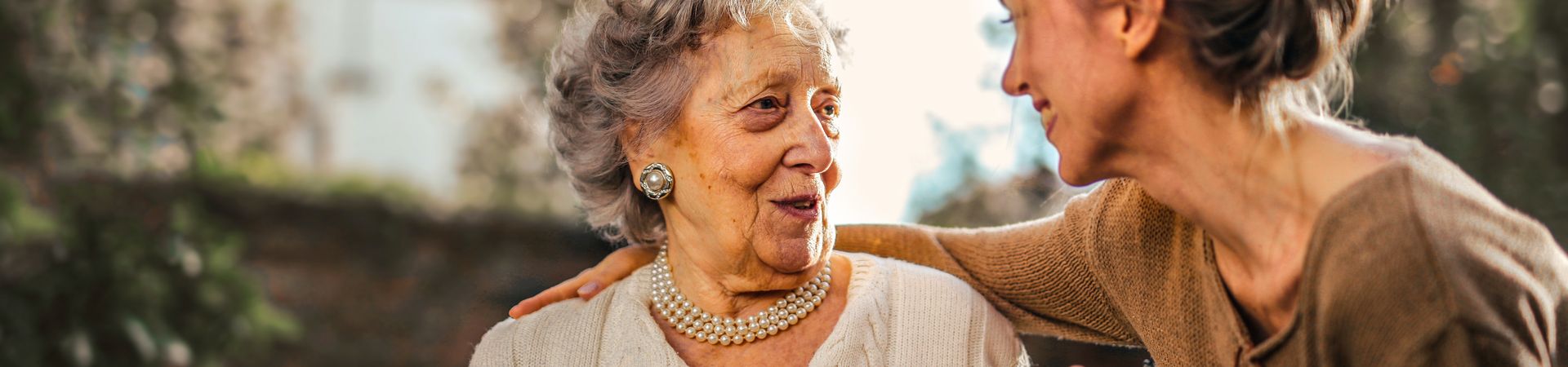 Jonge vrouw heeft arm om bejaarde vrouw heen en houdt haar hand vast