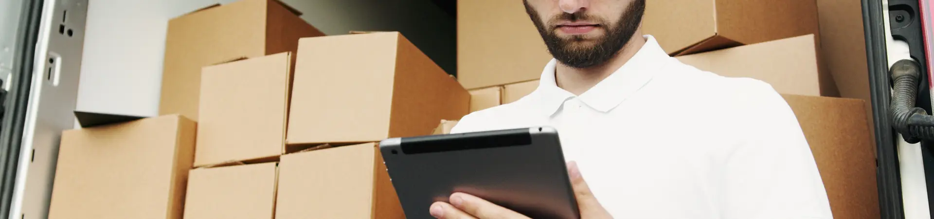 Pakketberzorgen kijkt op zijn iPad voor een bus vol met dozen