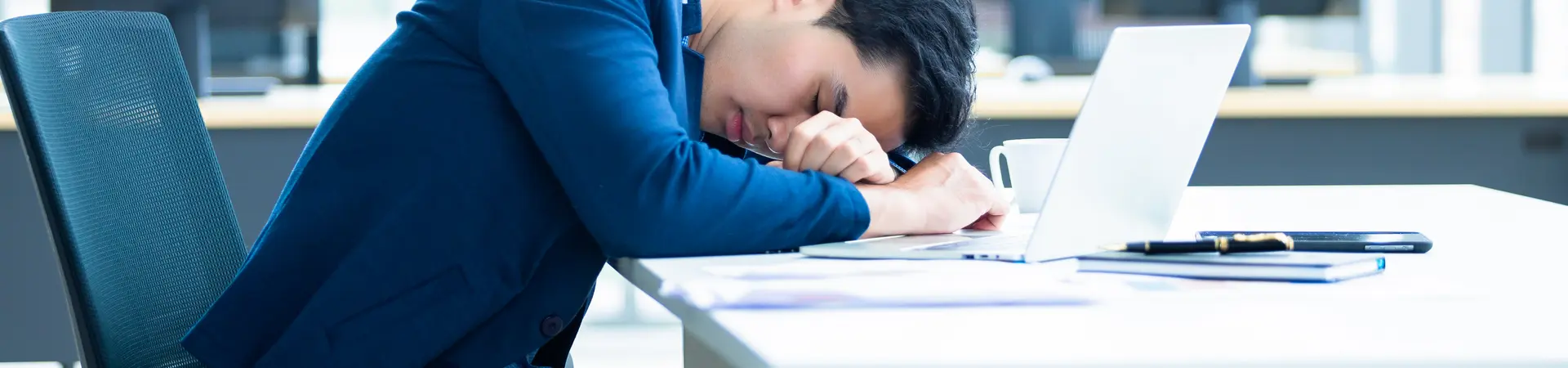 Zieke werknemer ligt tijdens werk op zijn witte bureau te leunen.  