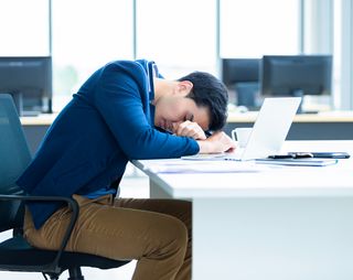 Zieke werknemer ligt tijdens werk op zijn witte bureau te leunen.