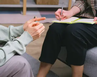 Twee mensen zitten tegenover elkaar in gesprek, waarvan er één notities maakt