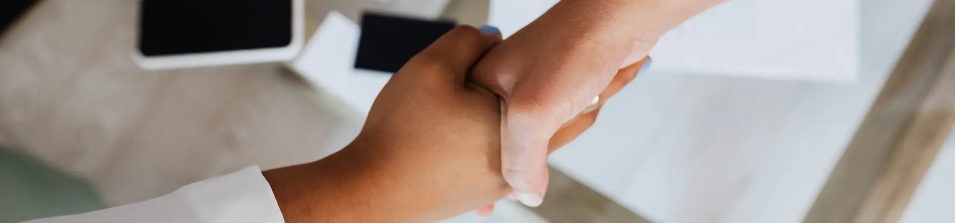 Twee handen schudden boven een laptop en een contract